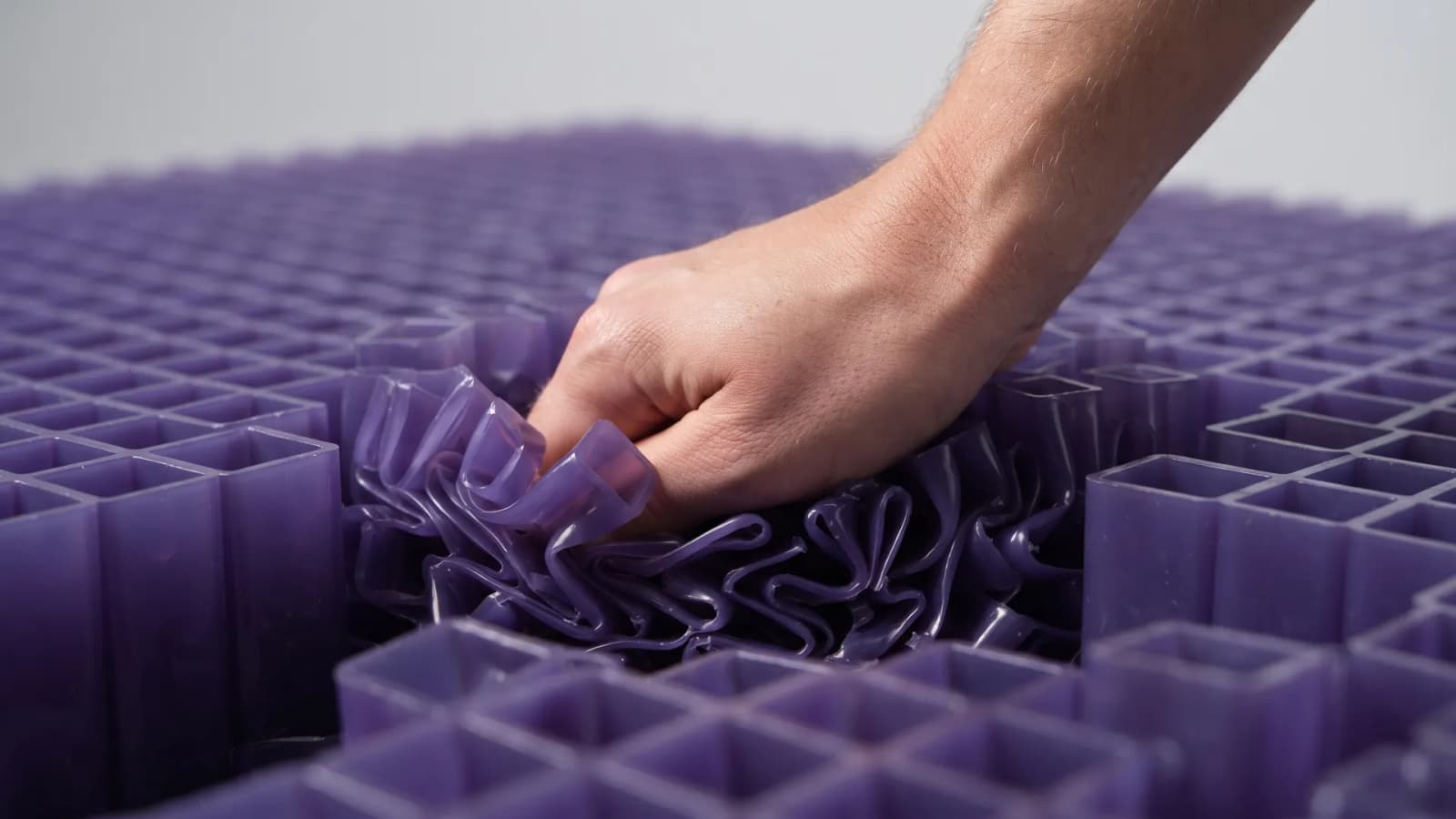 Close-up of a hand pressing into a purple polymer grid layer, with grid columns buckling under the palm