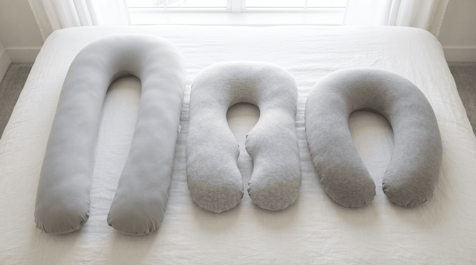 Overhead view of a gray 65-inch U pillow, a shorter contoured U pillow and a gray C-shaped pillow on white linen